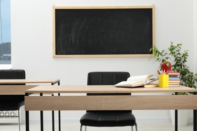 Photo of Different stationery and red apple on wooden table near blackboard indoors