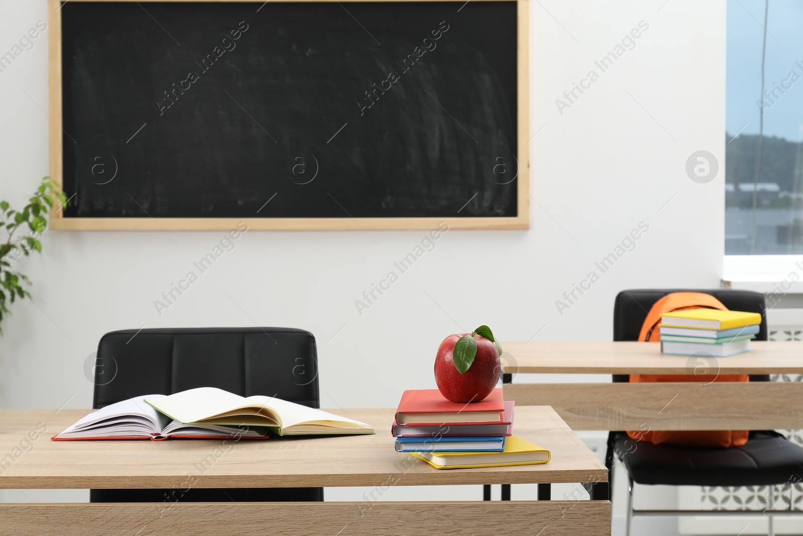 Different stationery and red apple on wooden table near blackboard indoors Photo of Different stationery and red apple on wooden table near blackboard indoors