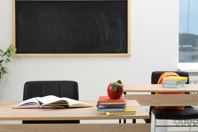 Photo of Different stationery and red apple on wooden table near blackboard indoors