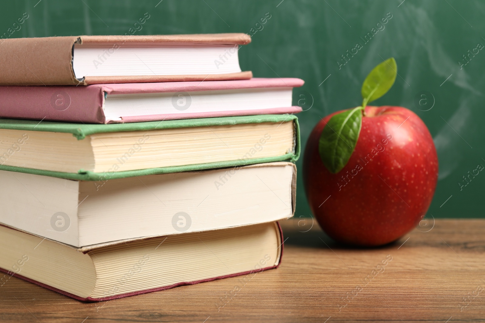 Different books and red apple on wooden table near blackboard, closeup Photo of Different books and red apple on wooden table near blackboard, closeup
