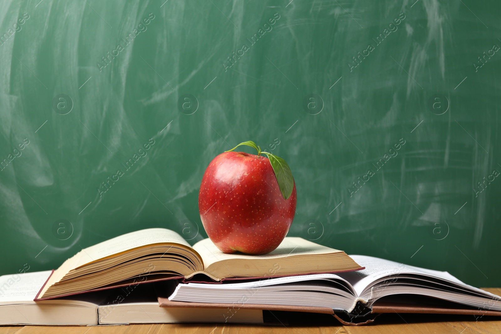 Different books and red apple on wooden table near blackboard Photo of Different books and red apple on wooden table near blackboard