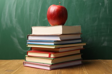 Photo of Different books and red apple on wooden table near blackboard