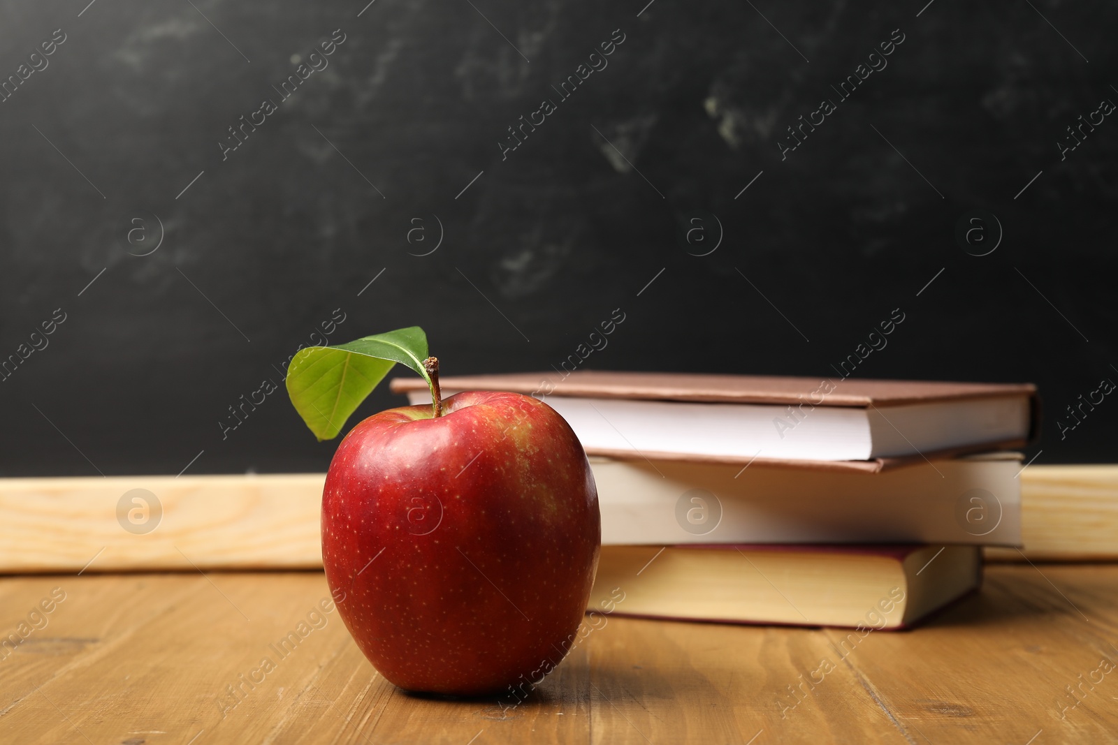 Different books and red apple on wooden table near blackboard Photo of Different books and red apple on wooden table near blackboard
