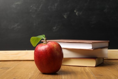 Photo of Different books and red apple on wooden table near blackboard