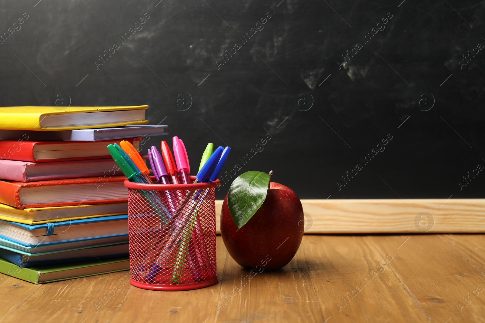 Different stationery and red apple on wooden table near blackboard, space for text Photo of Different stationery and red apple on wooden table near blackboard, space for text
