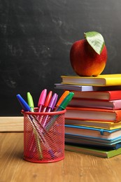 Photo of Different stationery and red apple on wooden table near blackboard