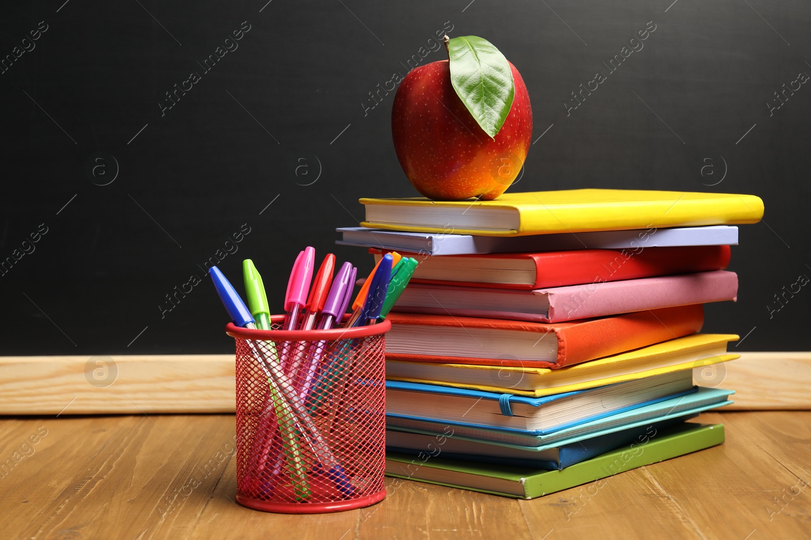 Different stationery and red apple on wooden table near blackboard Photo of Different stationery and red apple on wooden table near blackboard
