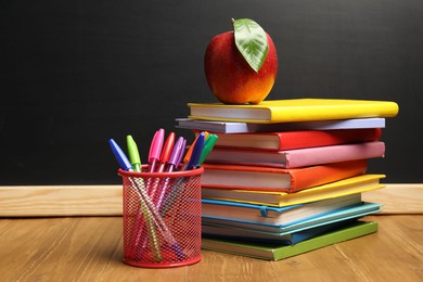 Photo of Different stationery and red apple on wooden table near blackboard