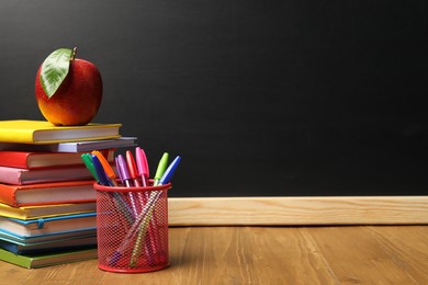 Photo of Different stationery and red apple on wooden table near blackboard, space for text