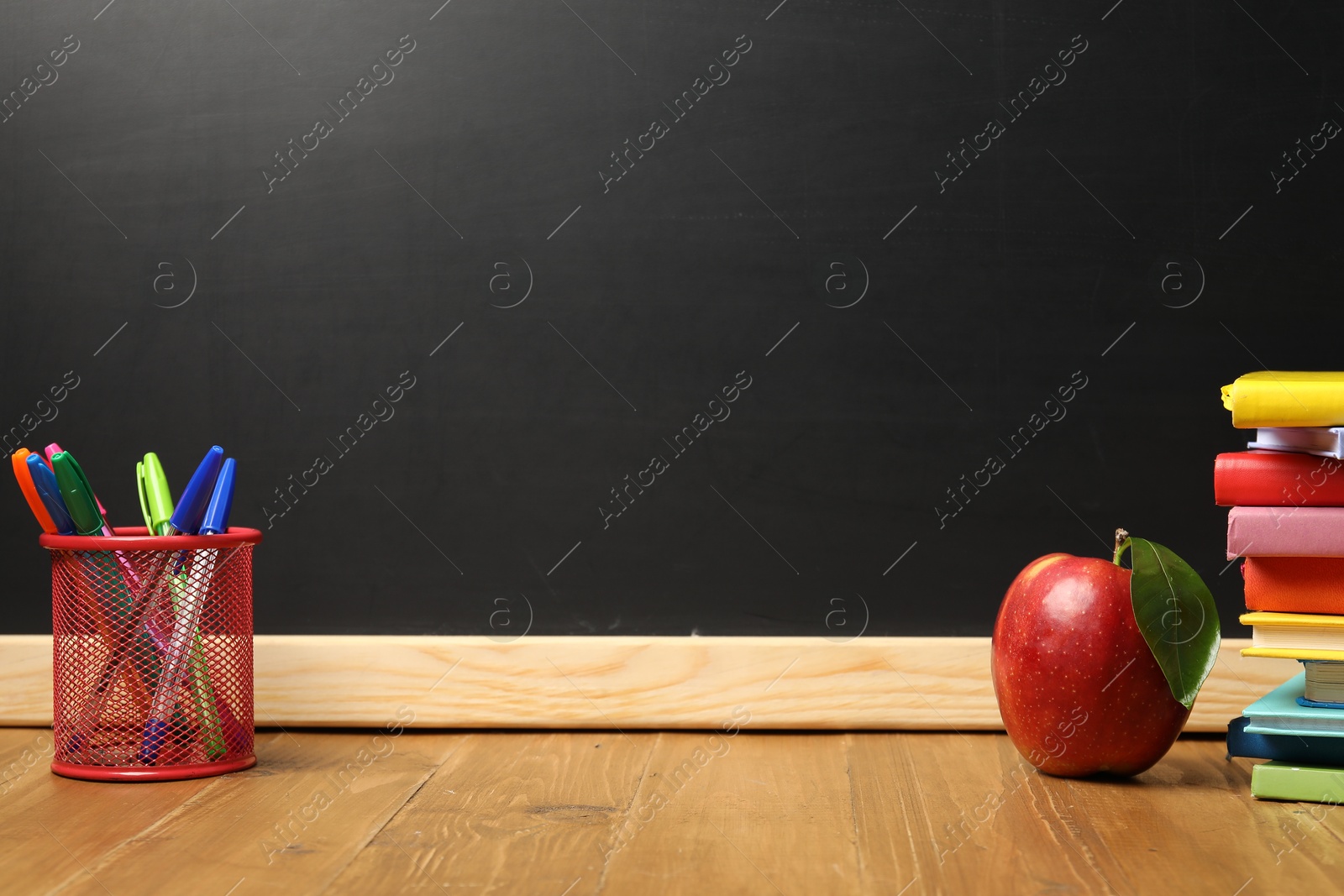 Different stationery and red apple on wooden table near blackboard, space for text Photo of Different stationery and red apple on wooden table near blackboard, space for text