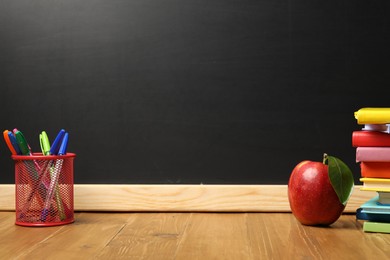 Photo of Different stationery and red apple on wooden table near blackboard, space for text