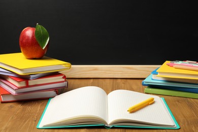 Photo of Different stationery and red apple on wooden table near blackboard
