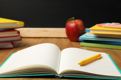 Photo of Different stationery and red apple on wooden table near blackboard, closeup