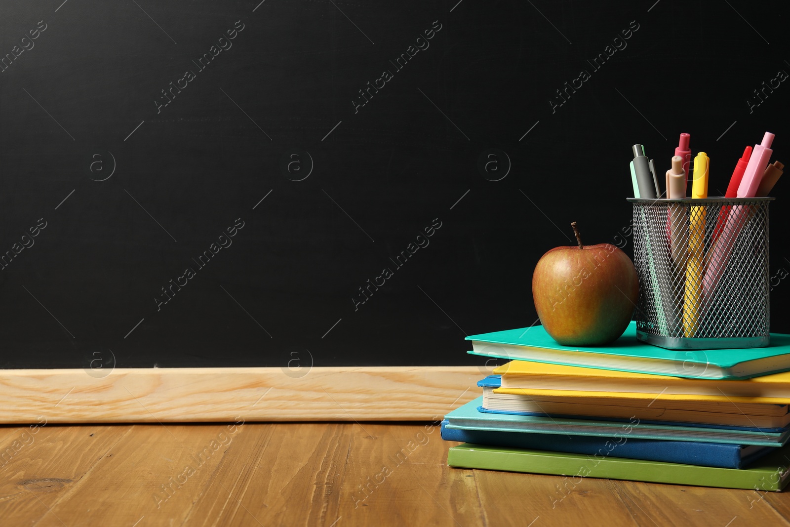Different stationery and apple on wooden table near blackboard, space for text Photo of Different stationery and apple on wooden table near blackboard, space for text