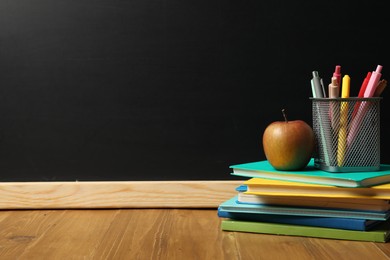 Photo of Different stationery and apple on wooden table near blackboard, space for text