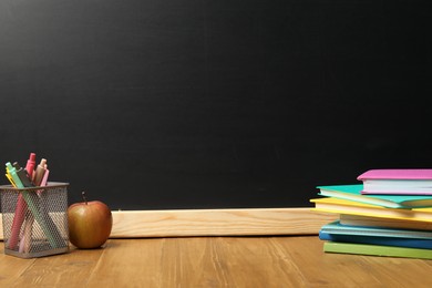 Photo of Different stationery and apple on wooden table near blackboard, space for text