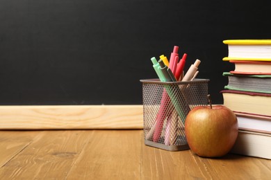 Photo of Different books, pens and apple on wooden table near blackboard, closeup. Space for text
