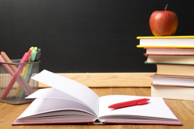 Photo of Different stationery and apple on wooden table near blackboard, closeup
