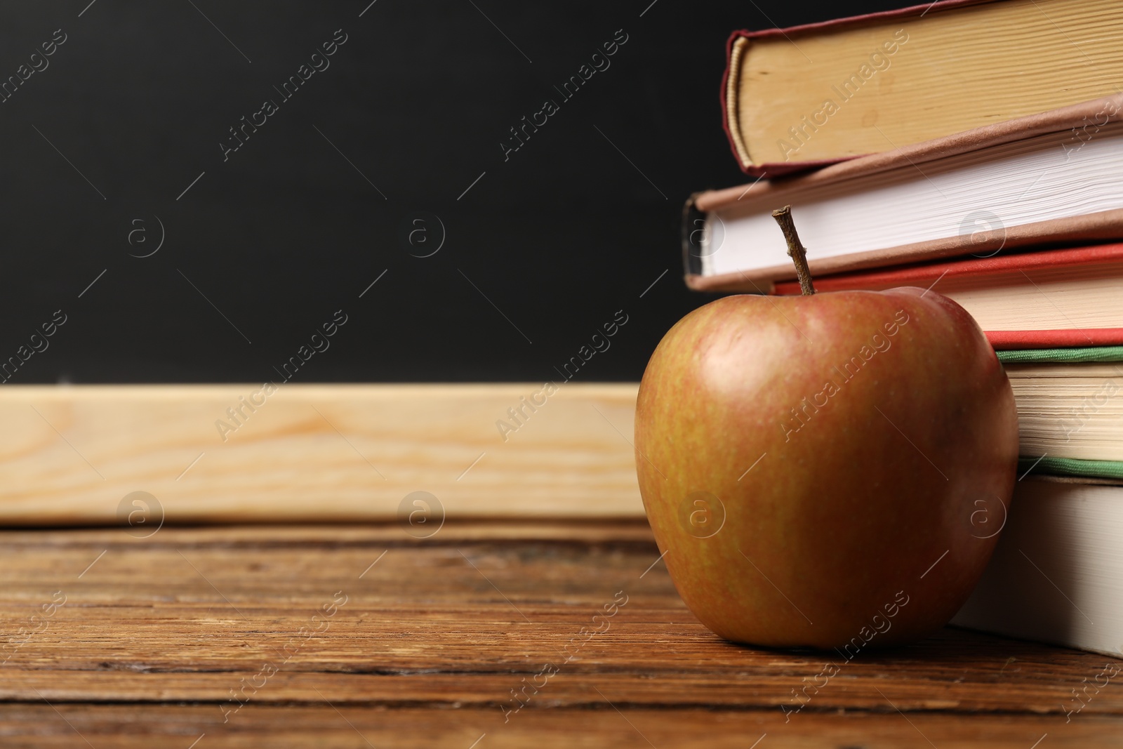 Different books and apple on wooden table near blackboard, closeup. Space for text Photo of Different books and apple on wooden table near blackboard, closeup. Space for text