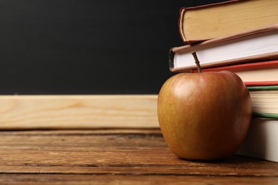 Photo of Different books and apple on wooden table near blackboard, closeup. Space for text