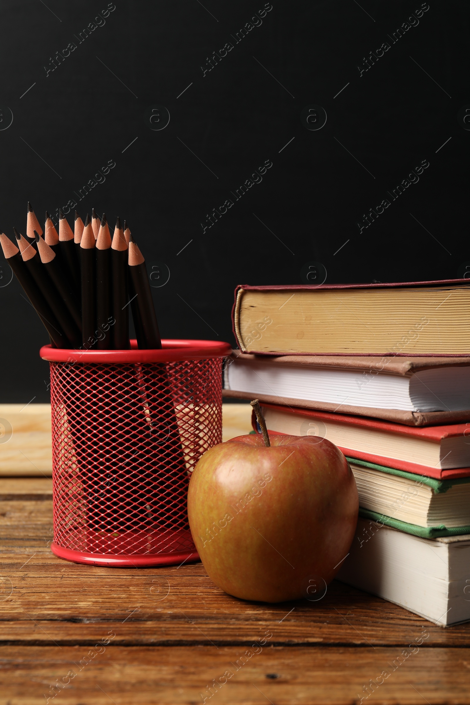 Different books, pencils and apple on wooden table near blackboard, closeup Photo of Different books, pencils and apple on wooden table near blackboard, closeup