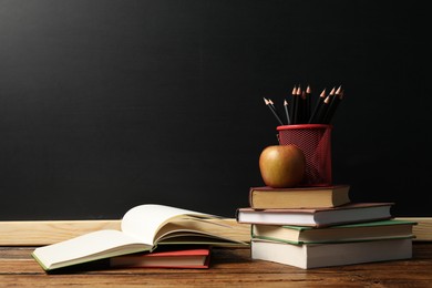 Photo of Different books, pencils and apple on wooden table near blackboard
