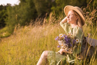 Photo of Woman with beautiful wildflowers, hat and backpack in meadow on sunny day. Space for text