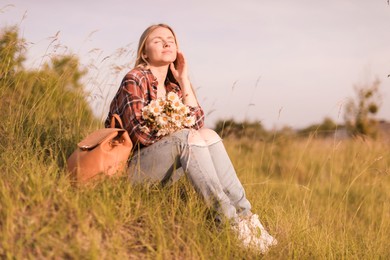 Photo of Beautiful woman with wildflowers and backpack enjoying summer day in meadow. Space for text