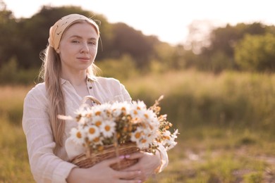 Photo of Happy woman with basket full of beautiful wildflowers outdoors