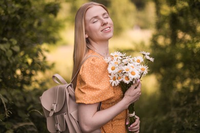 Photo of Beautiful woman with bouquet of wildflowers and backpack in forest