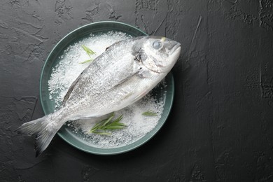 Photo of Organic seafood. Fresh raw dourade fish, salt and rosemary in bowl on black table, top view. Space for text