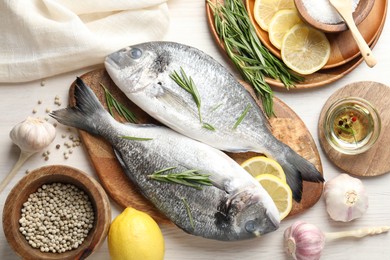 Photo of Fresh raw dourade fish, lemon slices, rosemary and spices on white wooden table, flat lay. Organic seafood