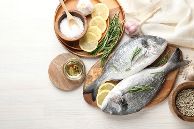 Photo of Organic seafood. Fresh raw dourade fish, lemon slices, rosemary and spices on white wooden table, flat lay. Space for text