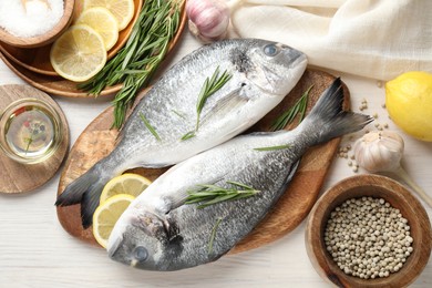 Photo of Fresh raw dourade fish, lemon slices, rosemary and spices on white wooden table, flat lay. Organic seafood