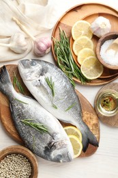 Photo of Fresh raw dourade fish, lemon slices, rosemary and spices on white wooden table, flat lay. Organic seafood