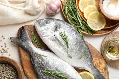 Photo of Fresh raw dourade fish, lemon slices, rosemary and spices on white wooden table, flat lay. Organic seafood