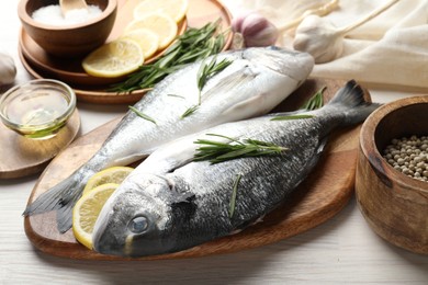 Photo of Fresh raw dourade fish, lemon slices, rosemary and spices on white wooden table, closeup. Organic seafood