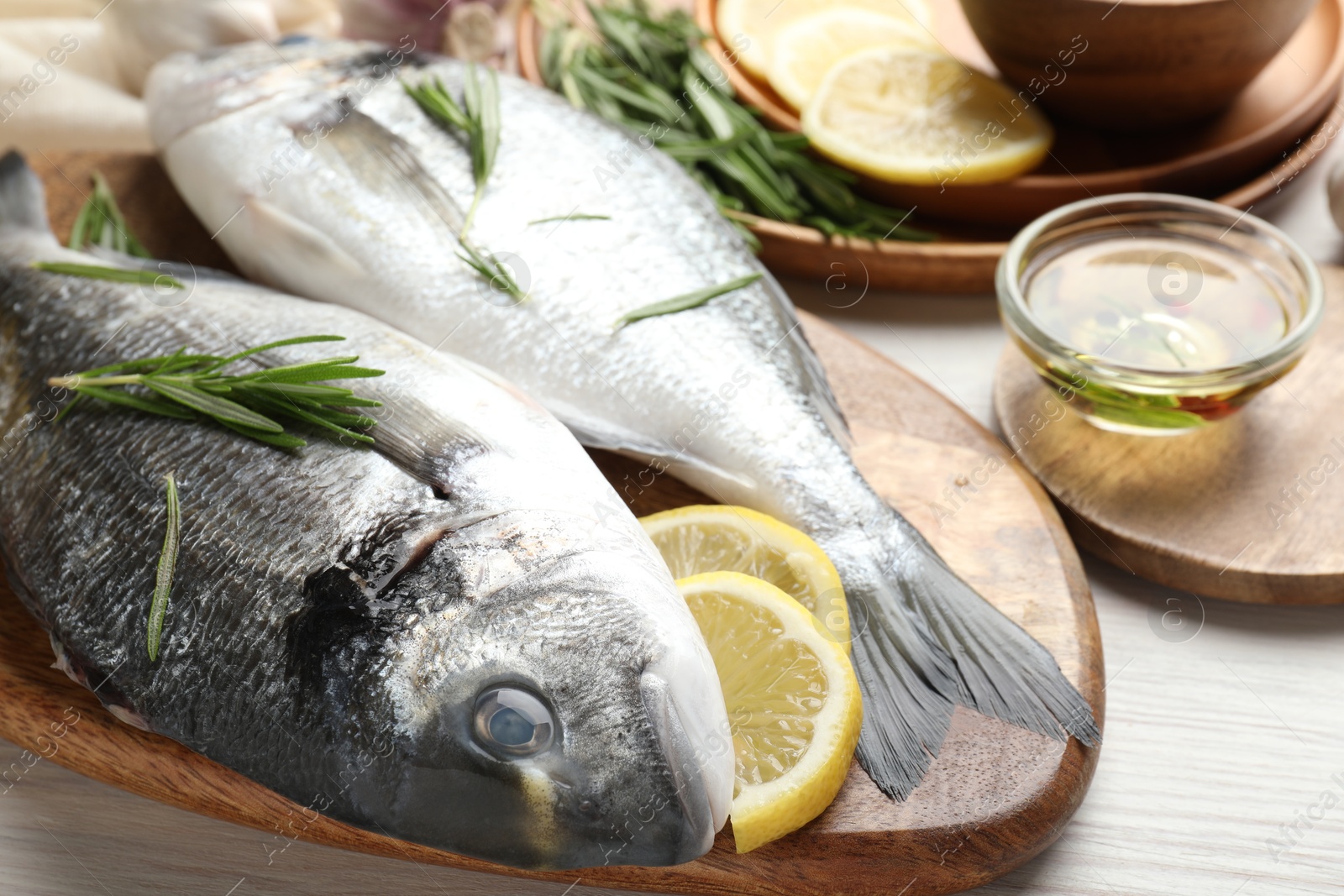 Fresh raw dourade fish, lemon slices, rosemary and spices on white wooden table, closeup. Organic seafood Photo of Fresh raw dourade fish, lemon slices, rosemary and spices on white wooden table, closeup. Organic seafood