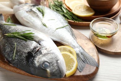 Photo of Fresh raw dourade fish, lemon slices, rosemary and spices on white wooden table, closeup. Organic seafood