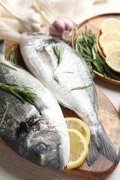 Photo of Fresh raw dourade fish, lemon slices, rosemary and spices on white wooden table, closeup. Organic seafood