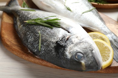 Photo of Fresh raw dourade fish, lemon slices, rosemary and spices on white wooden table, closeup. Organic seafood