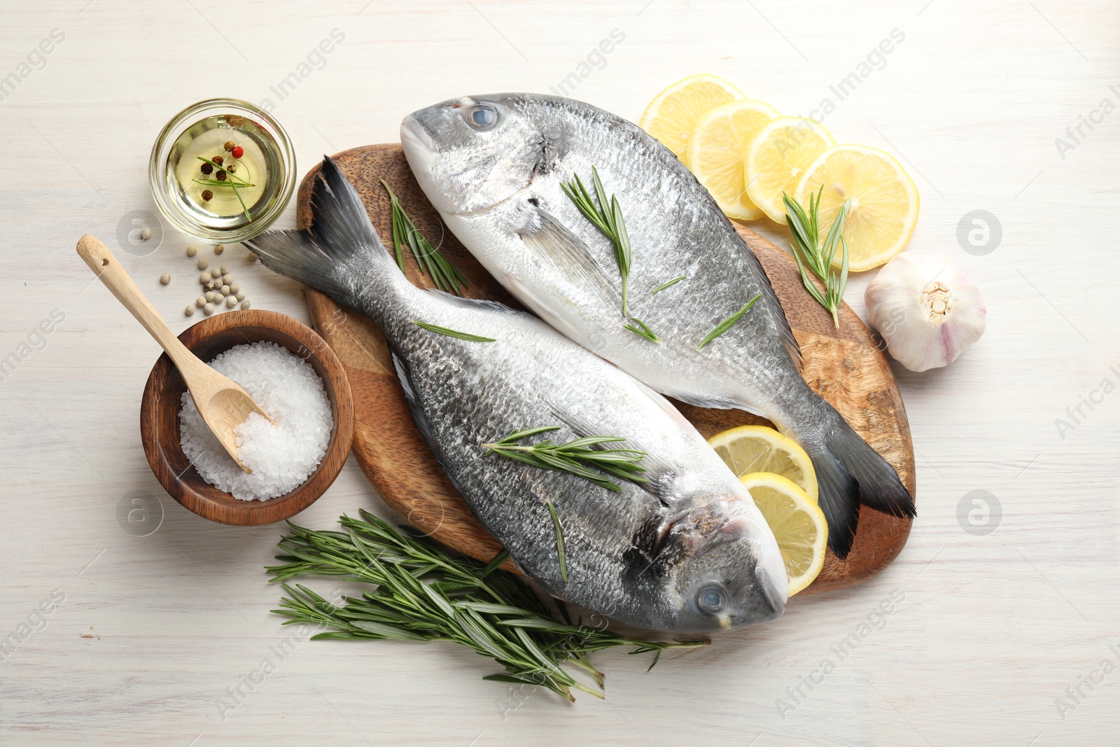 Fresh raw dourade fish, lemon slices, rosemary and spices on white wooden table, flat lay. Organic seafood Photo of Fresh raw dourade fish, lemon slices, rosemary and spices on white wooden table, flat lay. Organic seafood