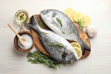 Photo of Fresh raw dourade fish, lemon slices, rosemary and spices on white wooden table, flat lay. Organic seafood