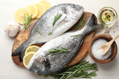 Photo of Fresh raw dourade fish, lemon slices, rosemary and spices on white wooden table, flat lay. Organic seafood