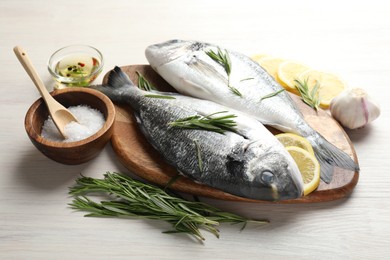 Photo of Fresh raw dourade fish, lemon slices, rosemary and spices on white wooden table, closeup. Organic seafood