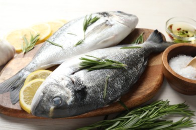 Photo of Fresh raw dourade fish, lemon slices, rosemary and spices on white wooden table, closeup. Organic seafood