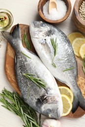 Photo of Fresh raw dourade fish, lemon slices, rosemary and spices on white wooden table, flat lay. Organic seafood