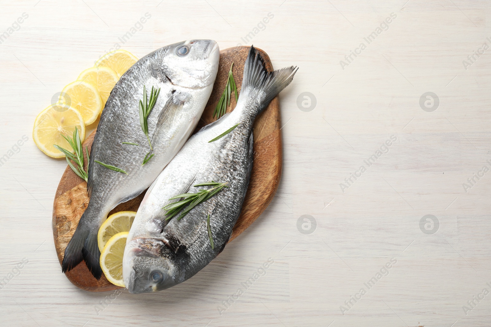Organic seafood. Fresh raw dourade fish, lemon slices and rosemary on white wooden table, flat lay. Space for text Photo of Organic seafood. Fresh raw dourade fish, lemon slices and rosemary on white wooden table, flat lay. Space for text