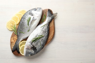 Photo of Organic seafood. Fresh raw dourade fish, lemon slices and rosemary on white wooden table, flat lay. Space for text