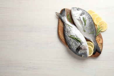 Photo of Organic seafood. Fresh raw dourade fish, lemon slices and rosemary on white wooden table, flat lay. Space for text